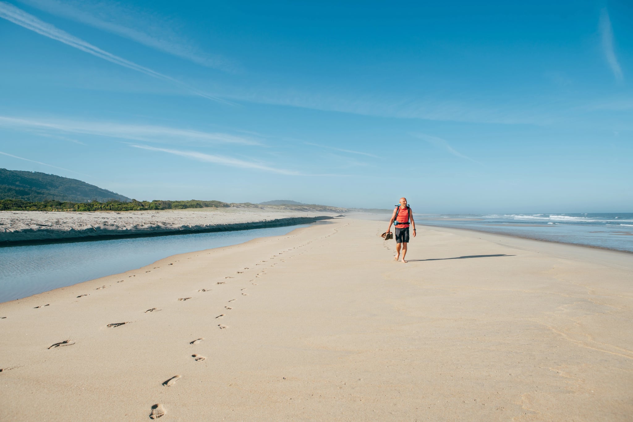 Samotny, boso wędrujący mężczyzna spacerujący po piaszczystej portugalskiej plaży rano na wybrzeżu Atlantyku. Zdjęcie z Camino Portugalskiego - popularnej trasy pielgrzymkowej. Aktywni ludzie, koncepcja podróżowania.