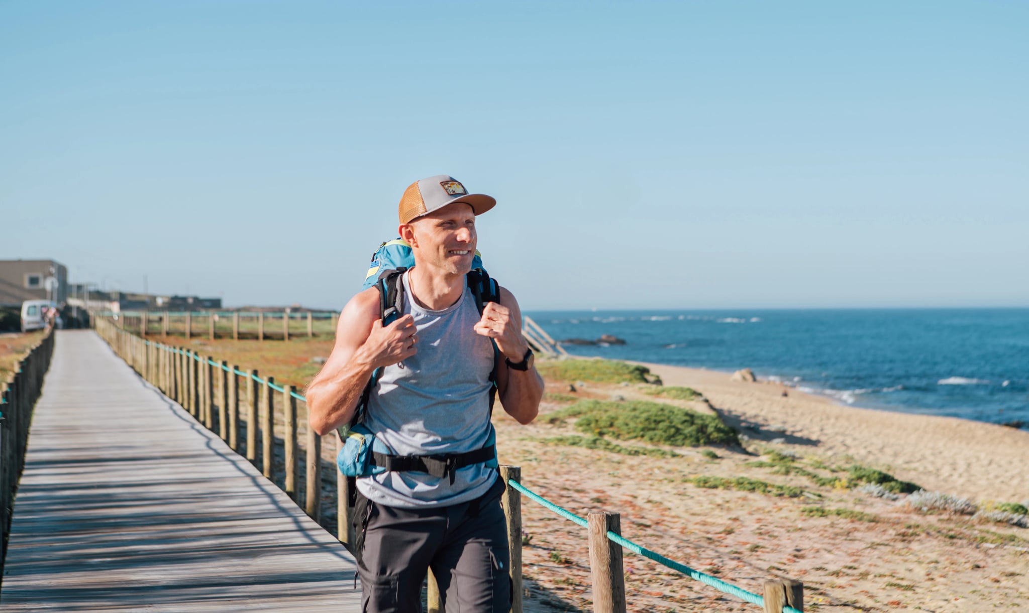 Samotny turysta uśmiechnięty mężczyzna idący po piaszczystej portugalskiej plaży rano. Ścieżka prowadząca przez drewniane pomosty wzdłuż wybrzeża oceanu. Zdjęcie z popularnej trasy pielgrzymkowej Camino Portuguese