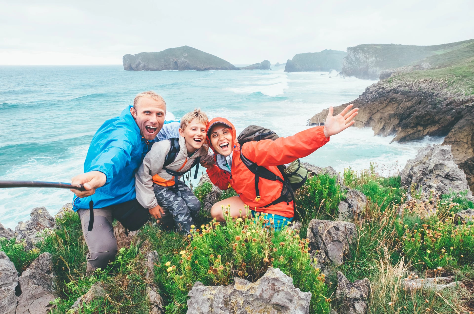 Happy travelers two parents family with their little son on the Cantabrian Sea coast cheerfully posing into camera as they going by Camino de Santiago way in Spain