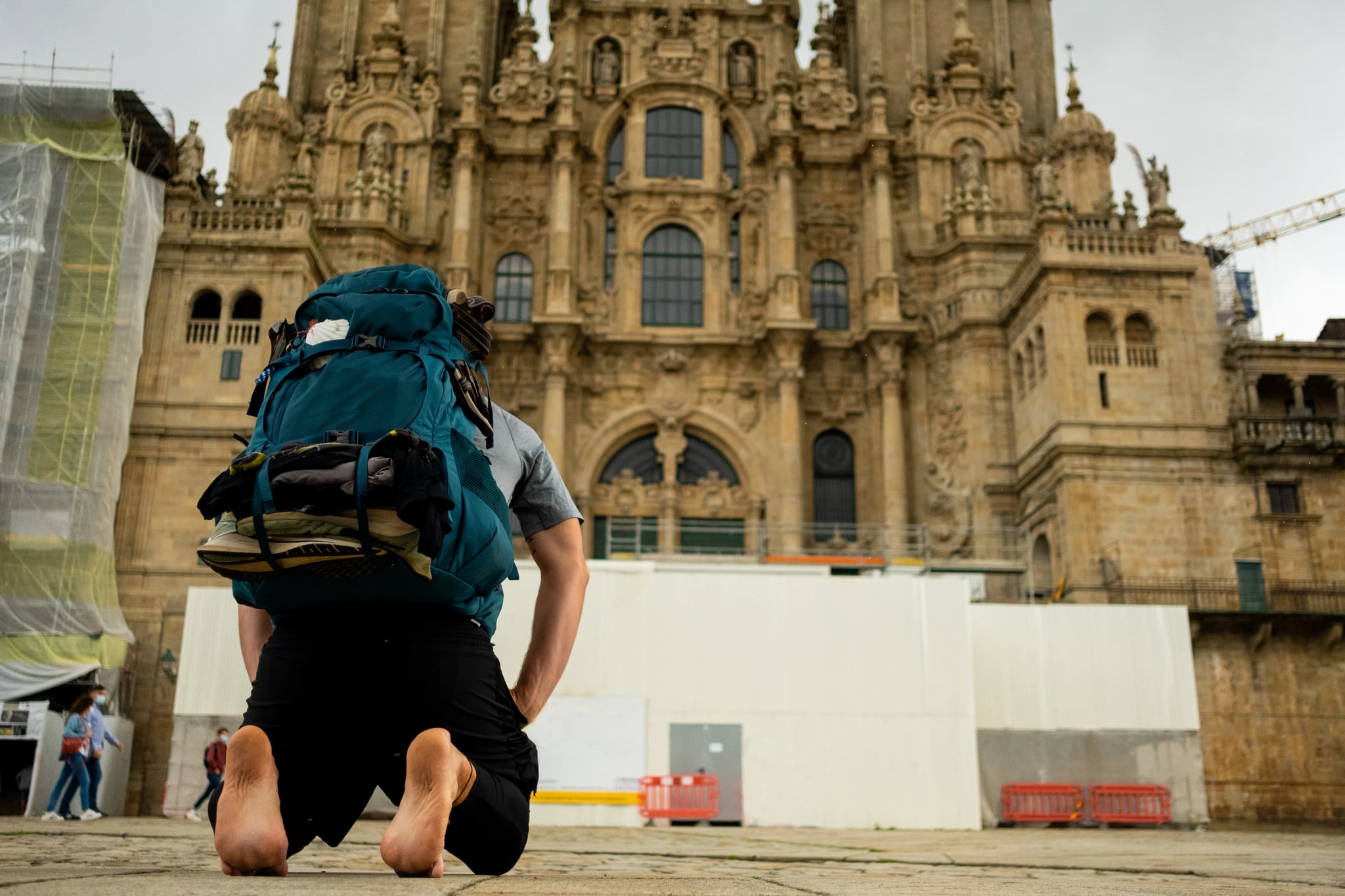pielgrzym Camino de Santiago klęczący przed katedrą Santiago po zakończeniu pielgrzymki, modlący się na boso na plaza del obradeiro