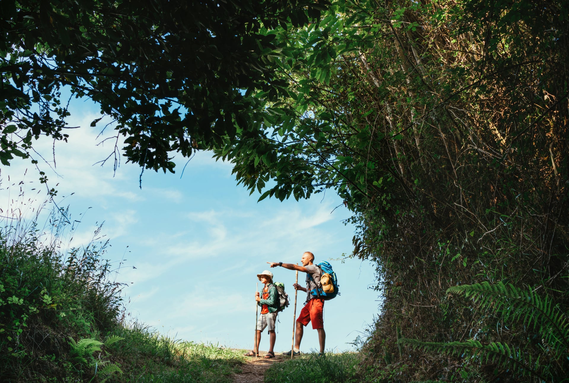 Father and son backpackers hiking by the forest pathway, taking a short rest break. Happy parents travelling with kids concept image.