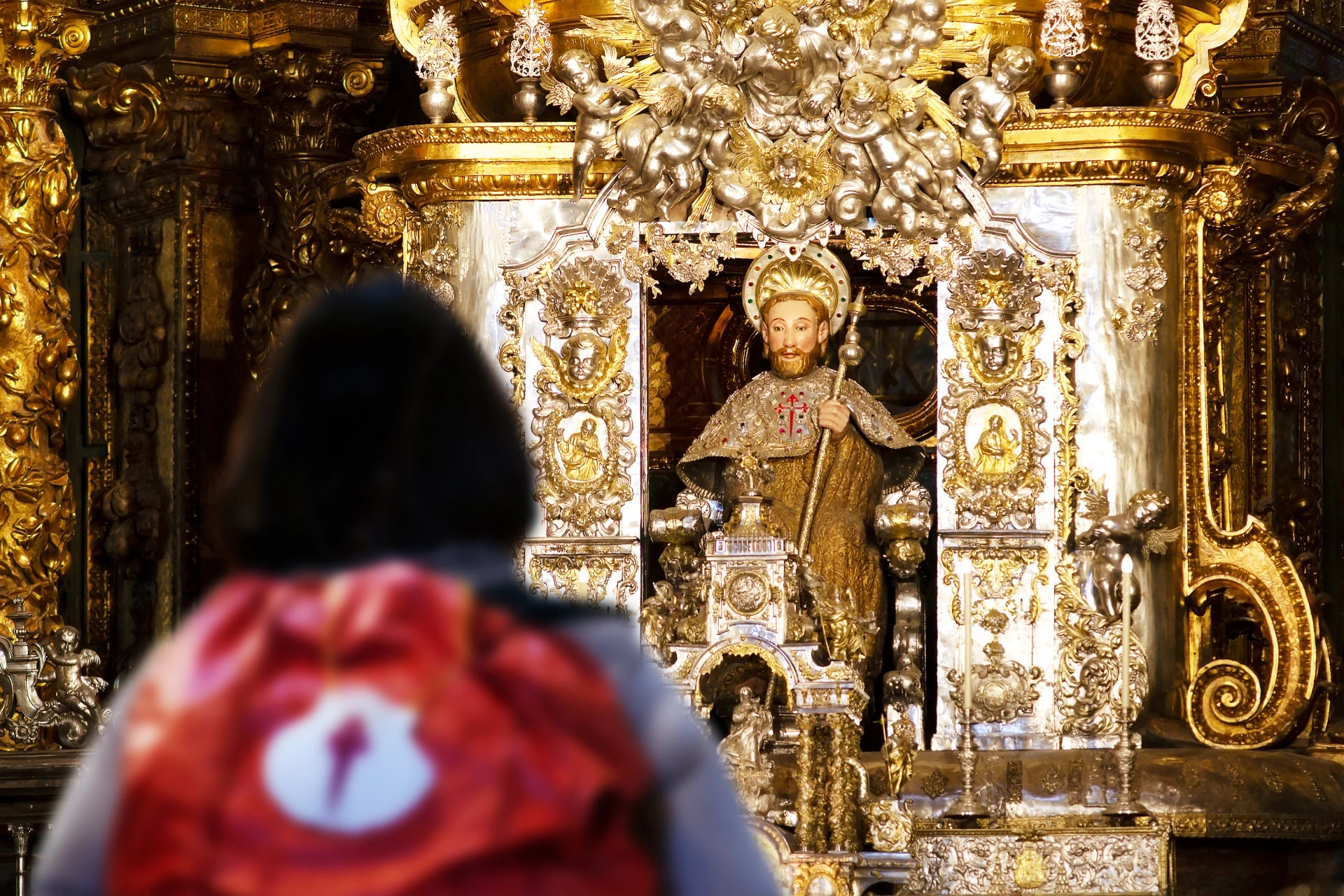 mulher peregrina desfocada que terminou o Caminho de Santiago até Compostela dentro da Catedral, com a imagem do apóstolo Santiago no altar