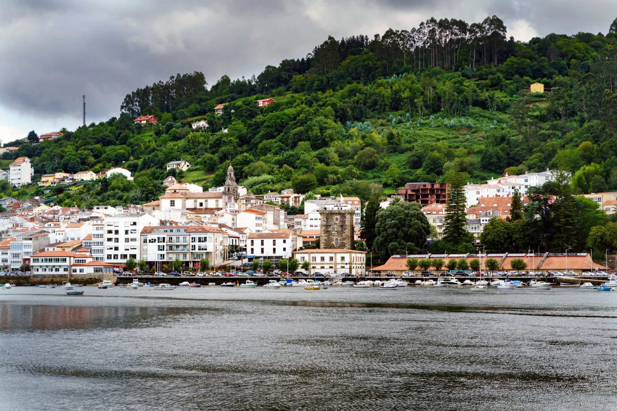 View of the town called Pontedeume in Galicia, Spain from the other side of the Eume estuary surrounded by a landscape with many trees and very green. Very cloudy sky threatening rain