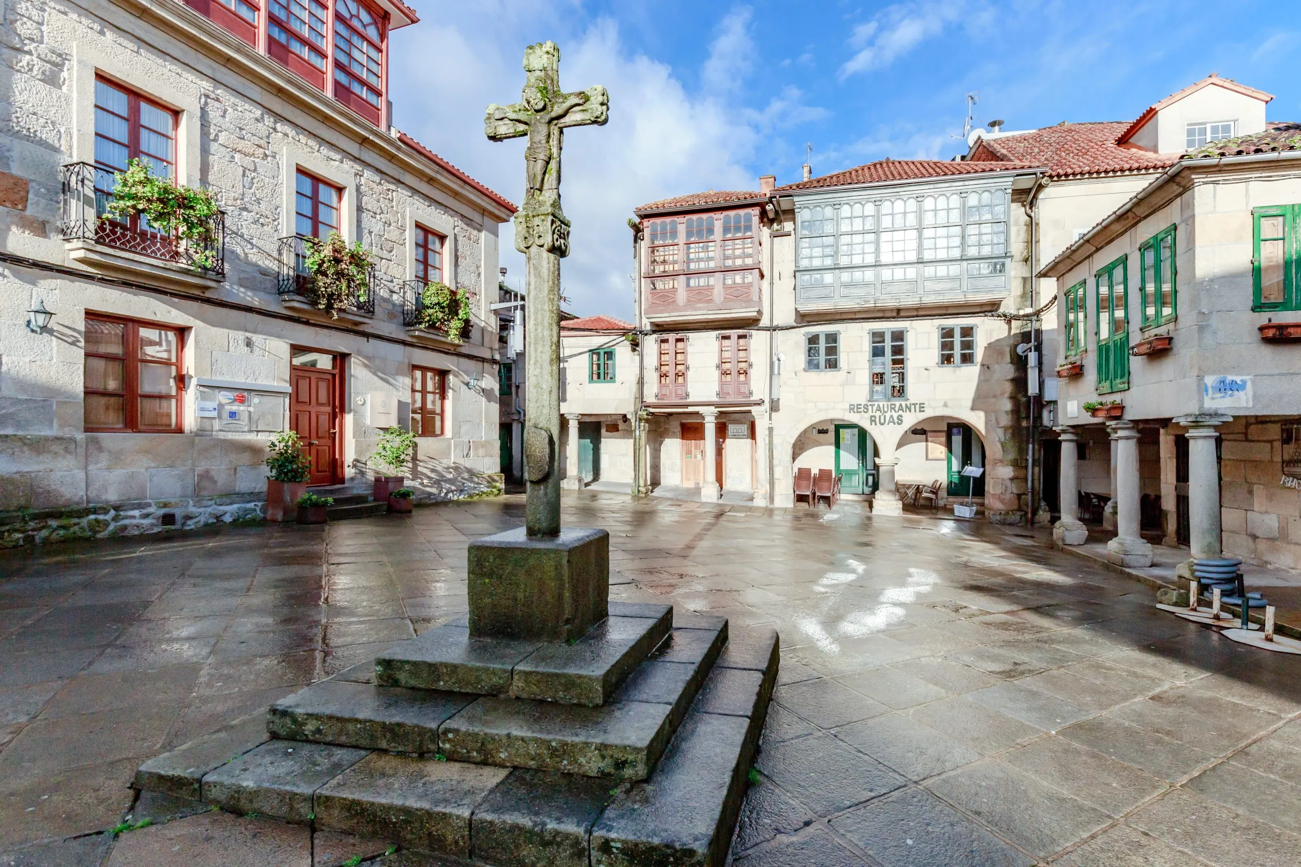 Spanien - Historischer Platz Praza da Lena in Pontevedra in Galicien. Gebäude mit farbiger Fassade, Holzfenstern, Balkonen und einem Steinkreuz in der Mitte.